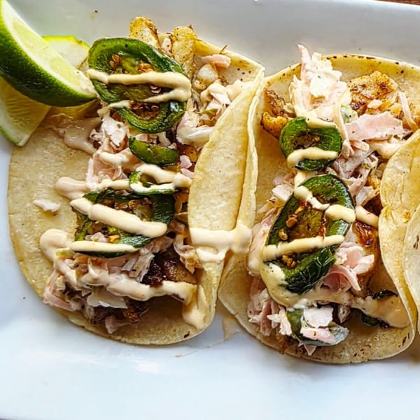 Two tacos with meat, cabbage, jalapeños, and sauce, served with lime wedges on a white plate.