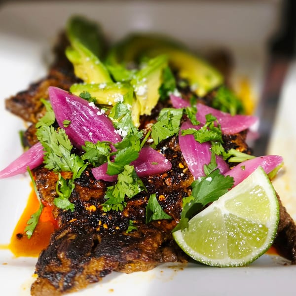 Grilled steak topped with avocado, pickled red onions, cilantro, and a lime wedge.