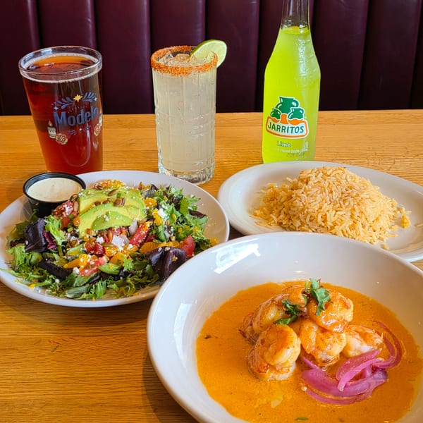 Table with shrimp in orange sauce, rice, salad with avocado, and three drinks.