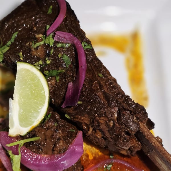 Close-up of a braised short rib with pickled red onions, cilantro, and a lime wedge.