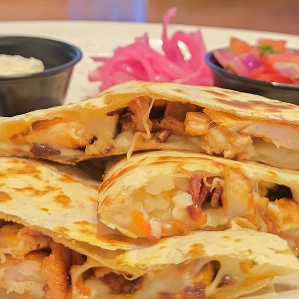 Close-up of golden-brown quesadillas filled with melted cheese, chicken, and bacon, served with sides.
