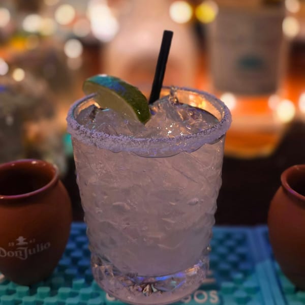 A refreshing margarita with a salted rim, lime wedge, and black straw, on a bar mat.