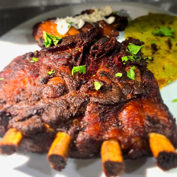 Close-up of barbecued ribs with cilantro, plantains, and a yellow tortilla on a white plate.